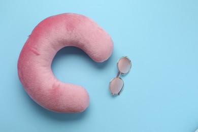 Photo of Pink travel pillow and sunglasses on light blue background, flat lay. Space for text