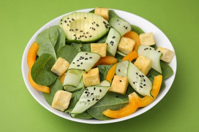 Bowl of tasty salad with tofu and vegetables on green background, closeup