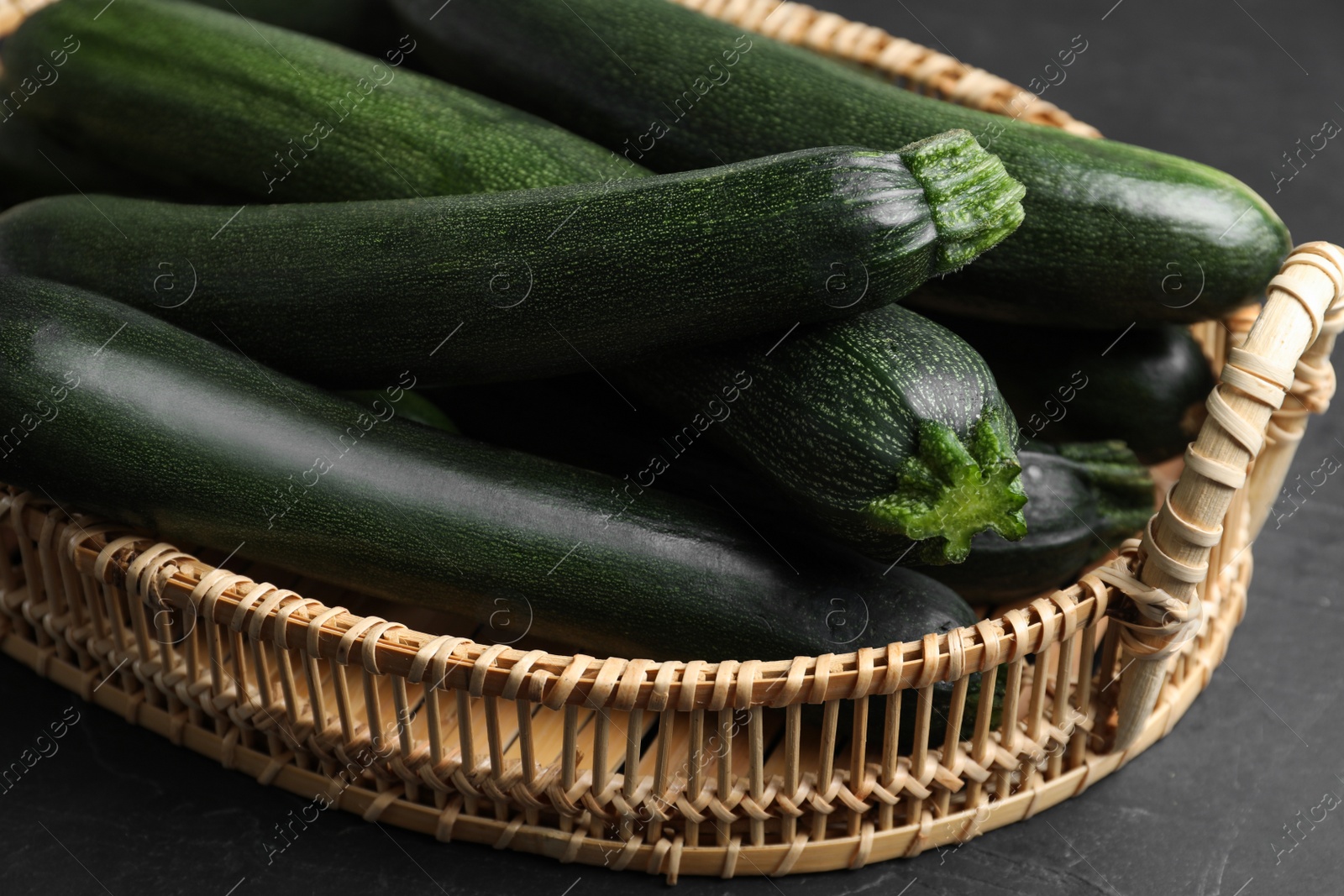 Photo of Basket with green zucchinis on black slate table, closeup