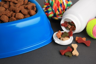 Bottle with vitamins, toys and dry pet food in bowl on grey background, closeup