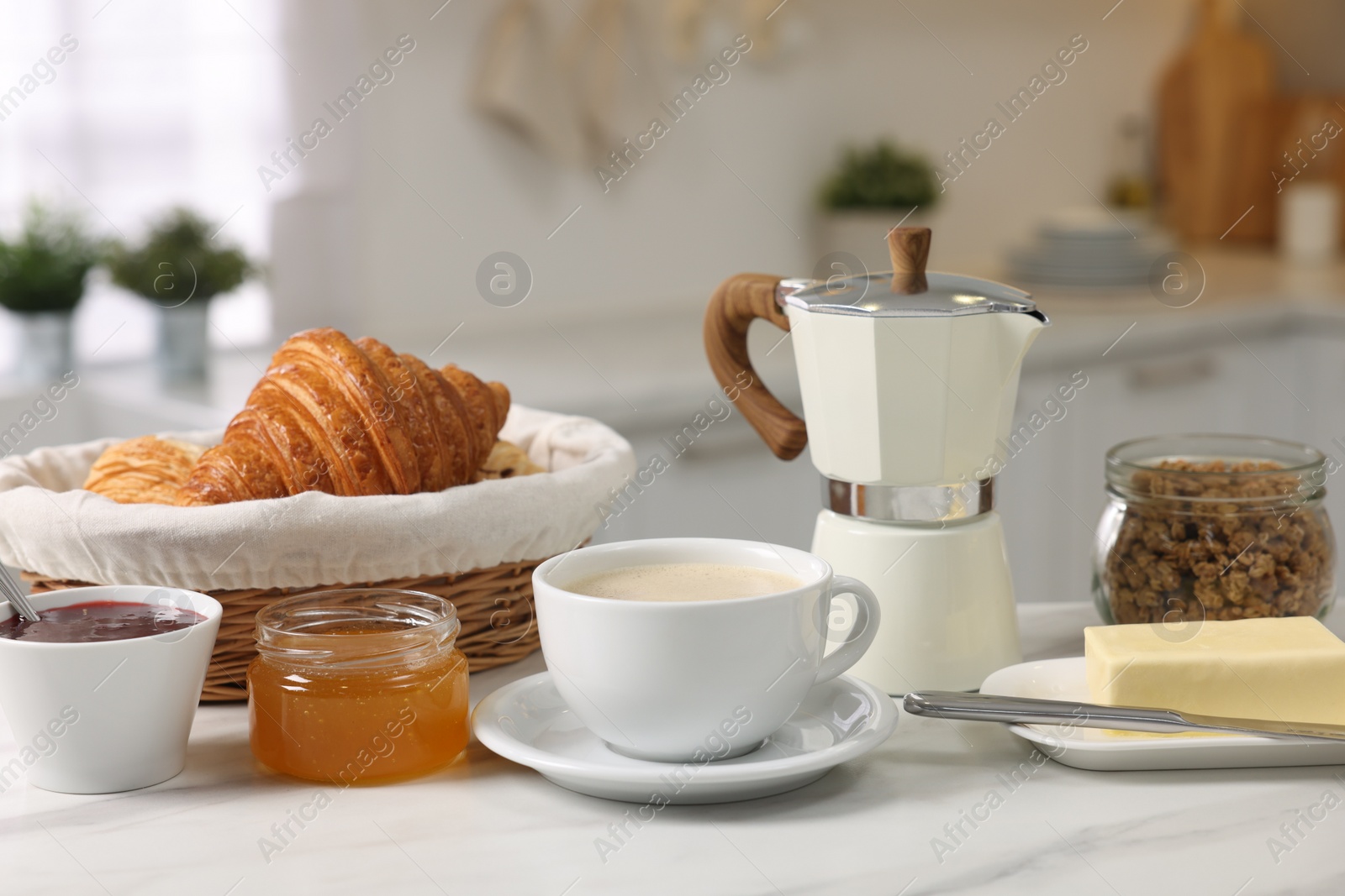 Photo of Breakfast served in kitchen. Fresh coffee, granola, croissants, jam, butter and honey on white table