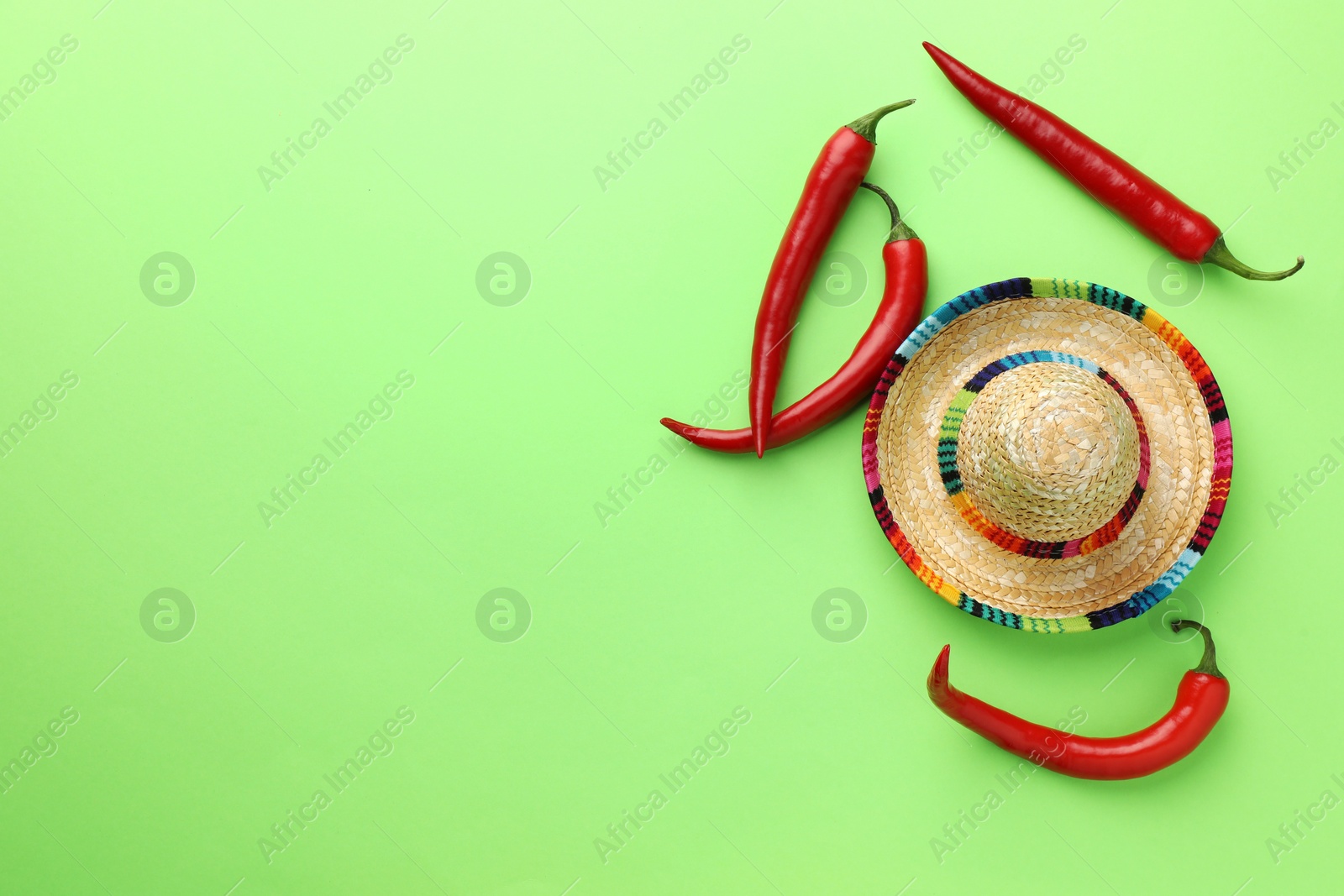 Photo of Mexican sombrero hat and chili peppers on green background, flat lay. Space for text