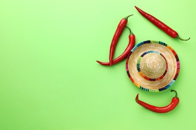 Photo of Mexican sombrero hat and chili peppers on green background, flat lay. Space for text