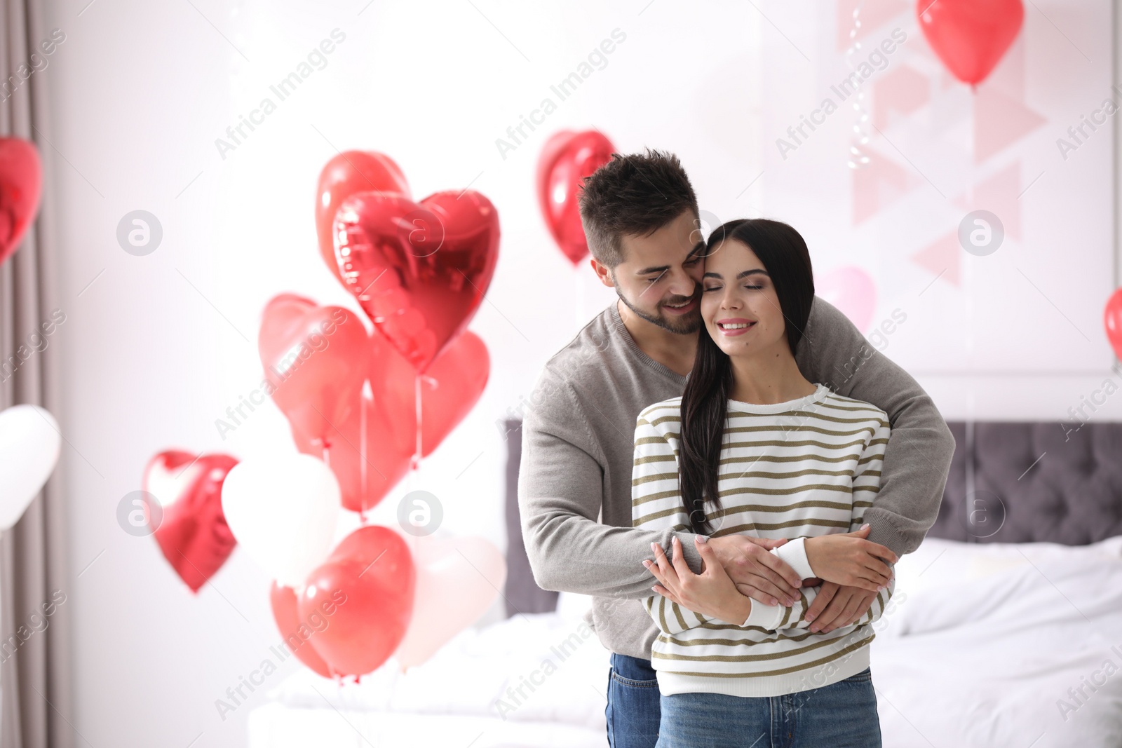 Photo of Lovely young couple in bedroom decorated with heart shaped balloons. Valentine's day celebration