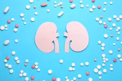 Paper cutout of kidneys and pills on light blue background, flat lay