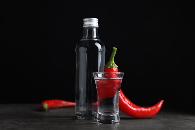 Photo of Red hot chili peppers and vodka on grey table against black background