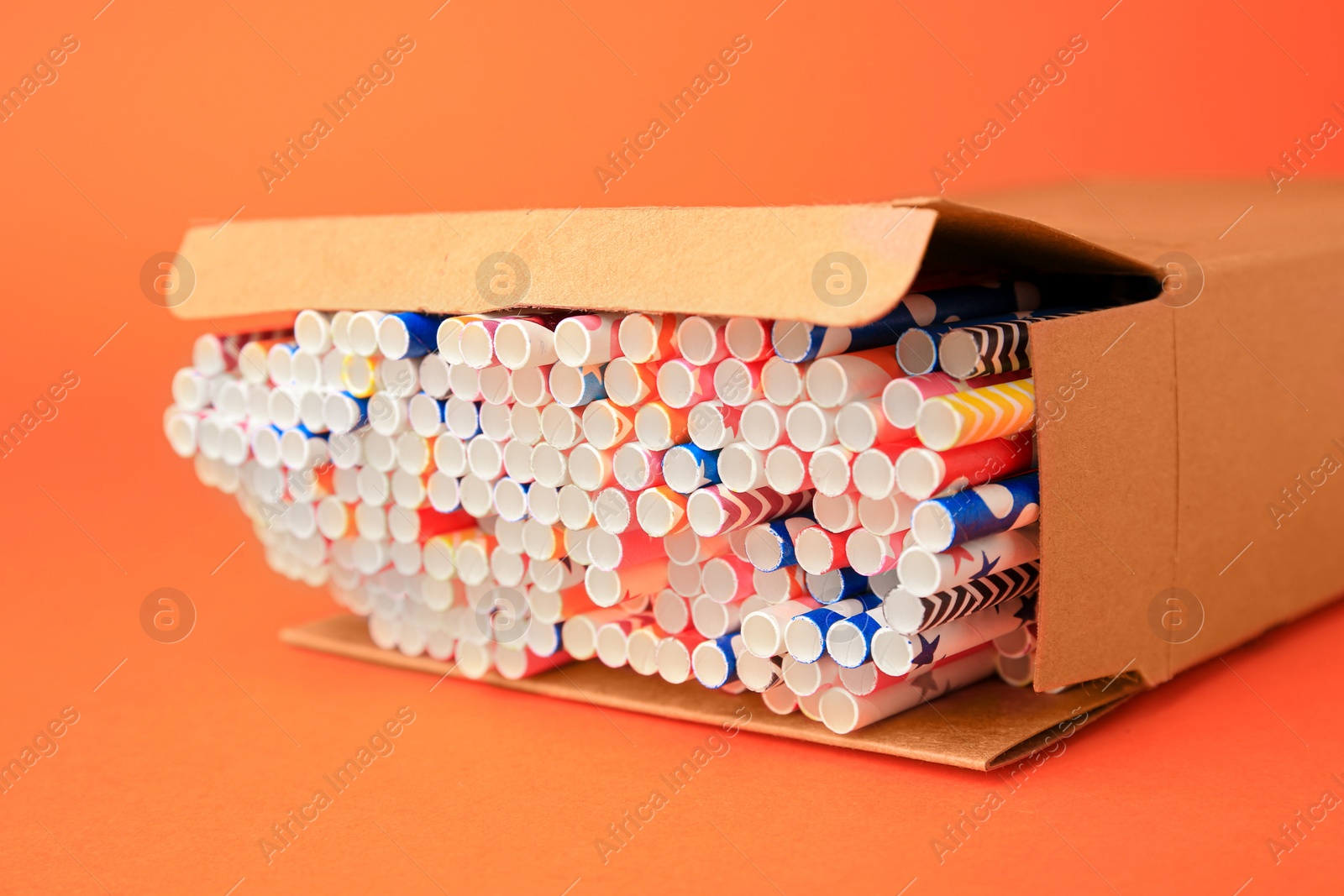 Photo of Box with many paper drinking straws on orange background