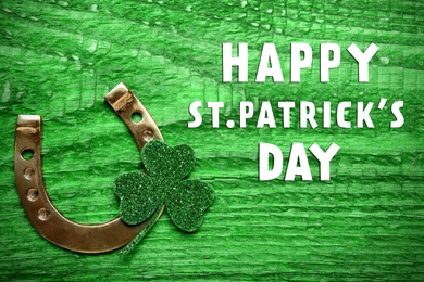 Image of Happy St. Patrick's Day. Golden horseshoe and decorative clover leaf on green wooden table, flat lay