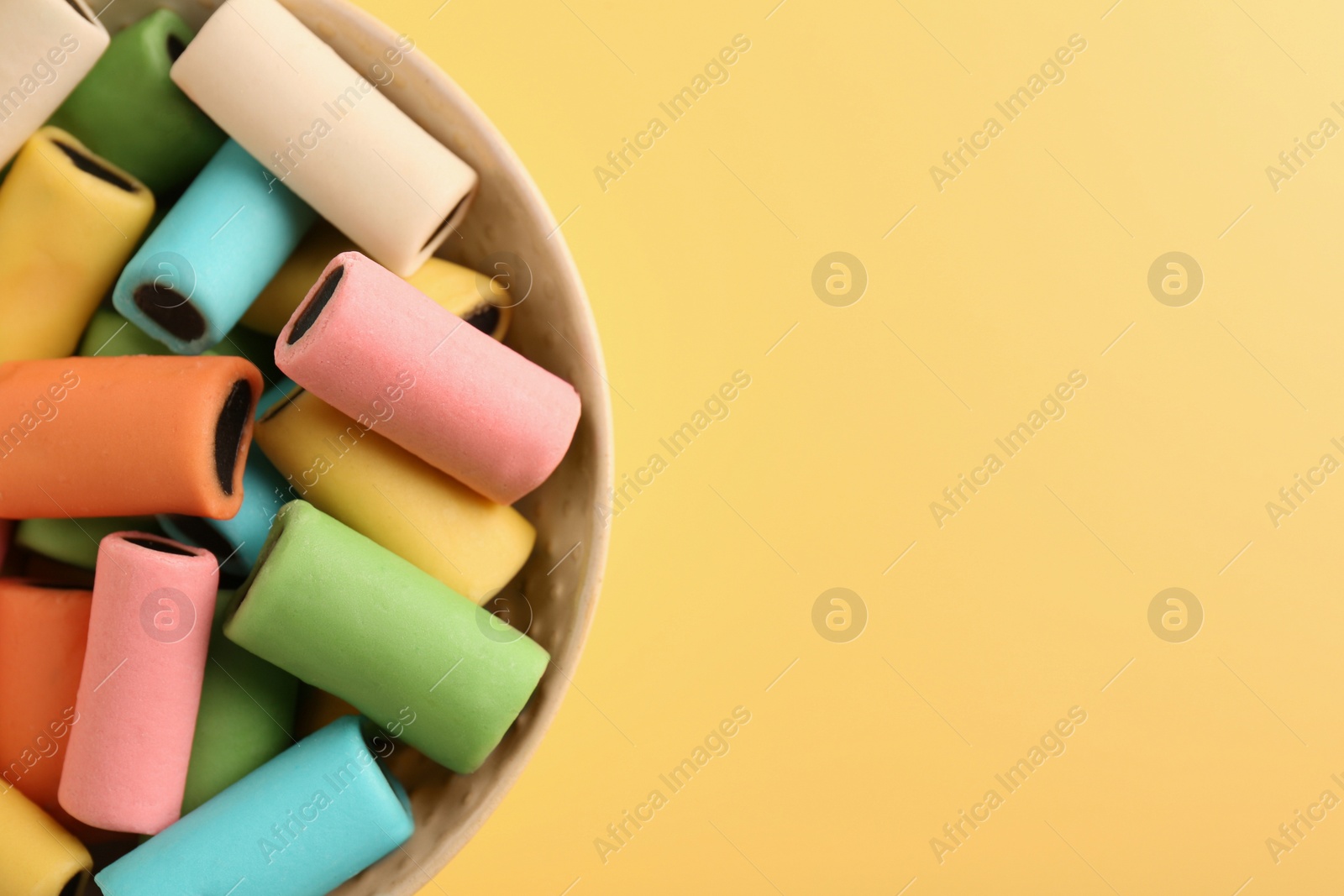 Photo of Bowl of tasty liquorice candies on yellow background, top view. Space for text