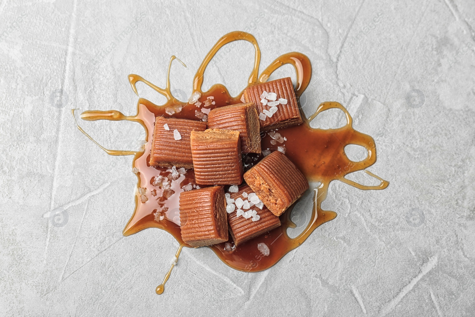 Photo of Delicious candies with caramel sauce and salt on light background, top view