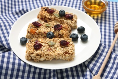 Photo of Tasty granola bars with berries served on checkered tablecloth