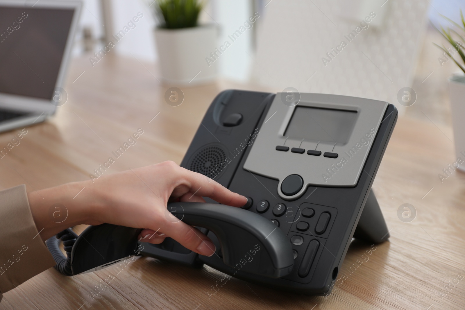 Photo of Woman using desktop telephone at wooden table in office, closeup. Hotline service