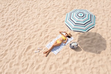 Image of Woman resting under striped beach umbrella at sandy coast