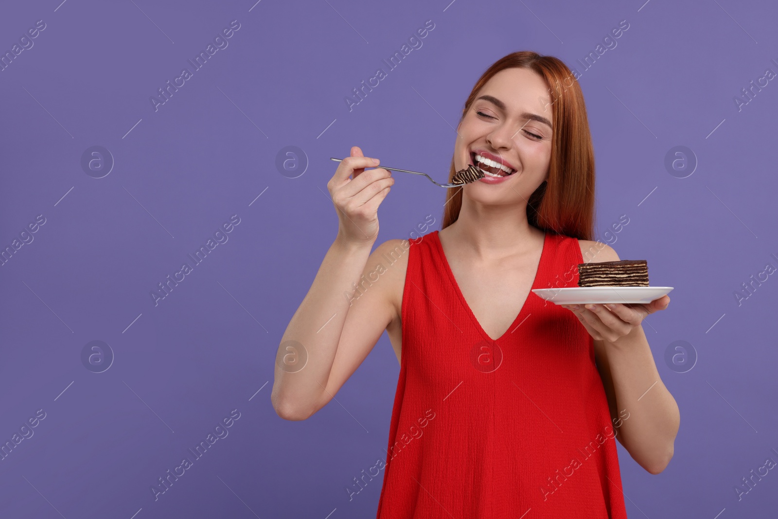 Photo of Young woman eating piece of tasty cake on purple background, space for text