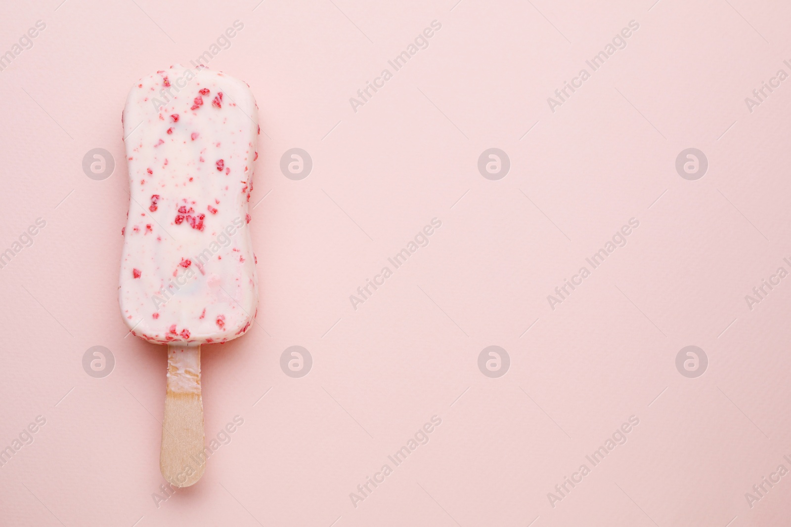 Photo of Delicious glazed ice cream bar on pale pink background, top view. Space for text