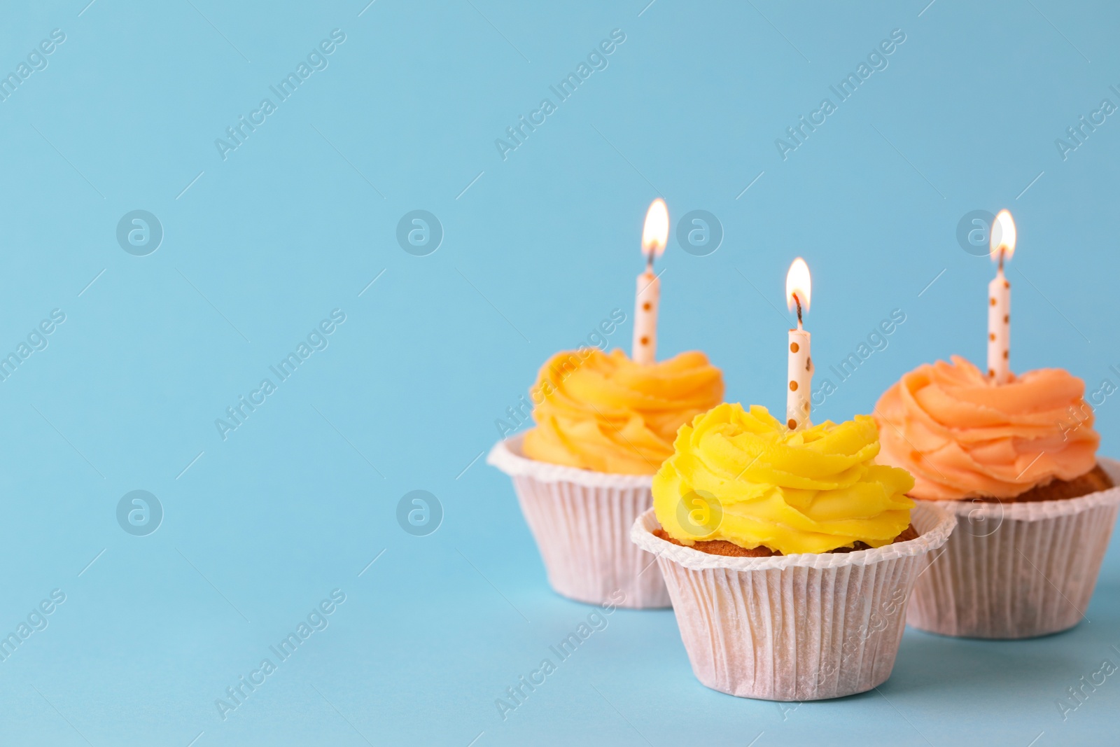 Photo of Tasty birthday cupcakes with candles on light blue background. Space for text