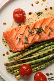 Tasty grilled salmon with tomatoes, asparagus and spices on plate, top view