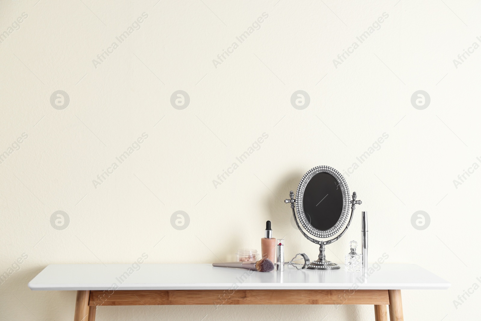 Photo of Mirror and makeup products on white table near light wall. Space for text