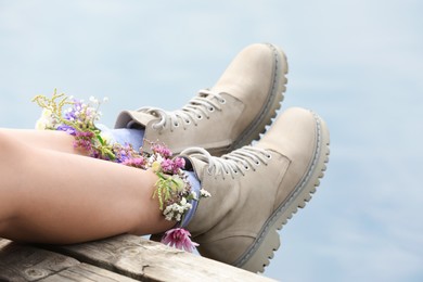 Photo of Woman sitting on wooden pier with flowers in socks outdoors, closeup