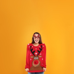 Young woman in Christmas sweater and party glasses on yellow background, space for text