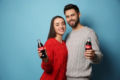 Photo of MYKOLAIV, UKRAINE - JANUARY 27, 2021: Young couple holding bottles of Coca-Cola on light blue background
