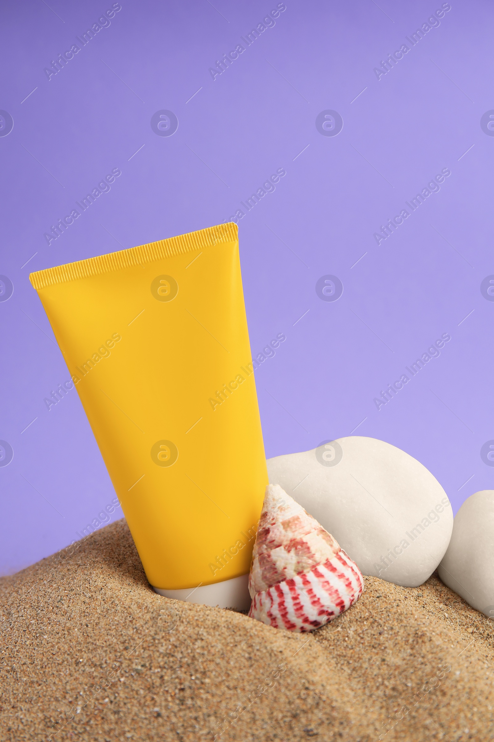 Photo of Sand with sunscreen, stones and seashell against lilac background, space for text. Sun protection care