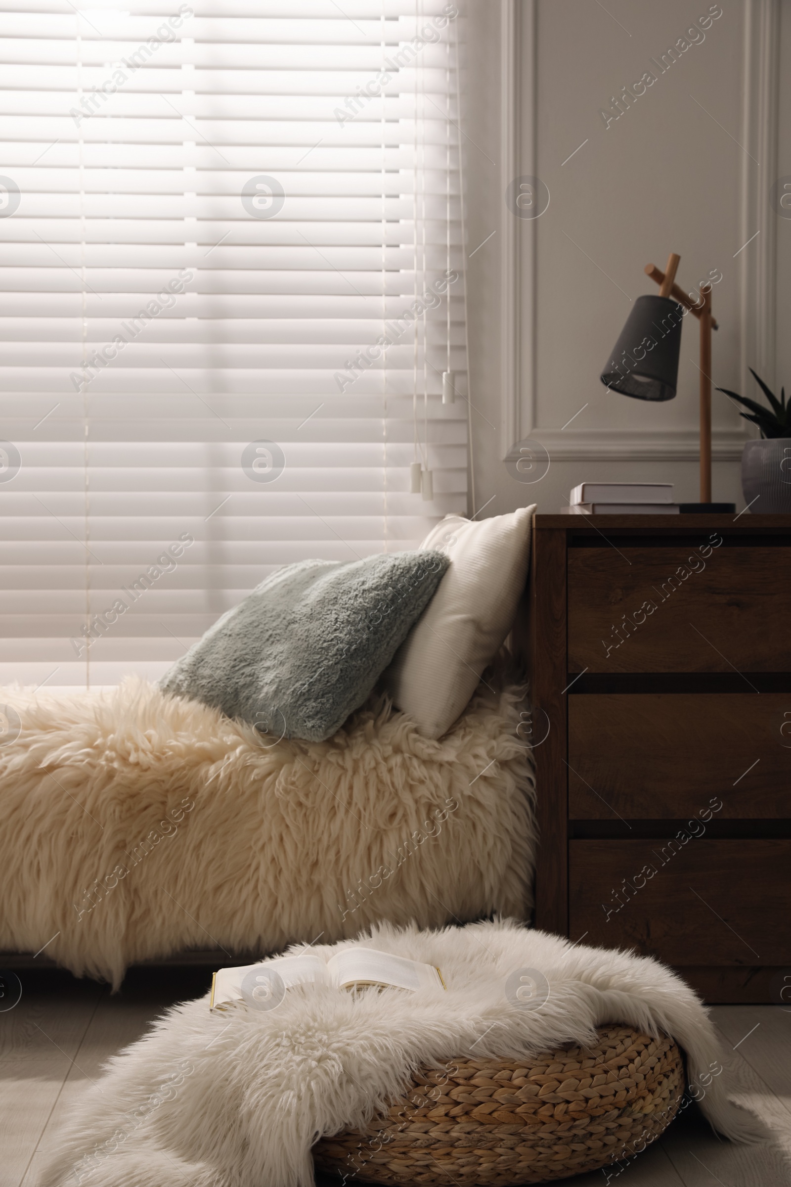 Photo of Comfortable place for relax with faux fur and pillows near window in room