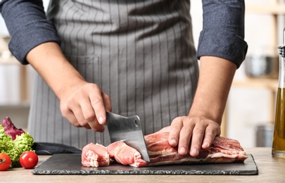 Photo of Man cutting fresh raw meat on wooden table in kitchen, closeup