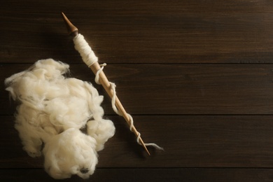 Photo of Soft white wool with spindle on wooden table, flat lay. Space for text