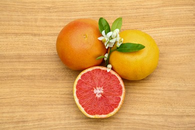 Photo of Fresh ripe grapefruits, flowers and green leaves on wooden table, top view