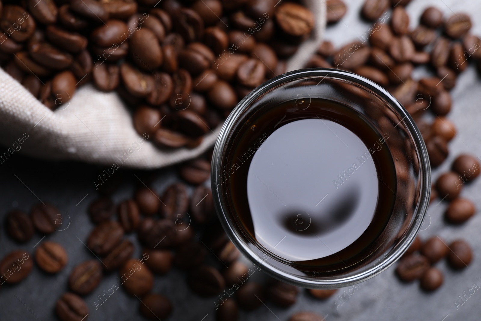 Photo of Glass of coffee liqueur and beans on grey table, top view. Space for text
