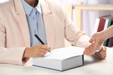 Photo of Writer signing autograph in book at table, closeup