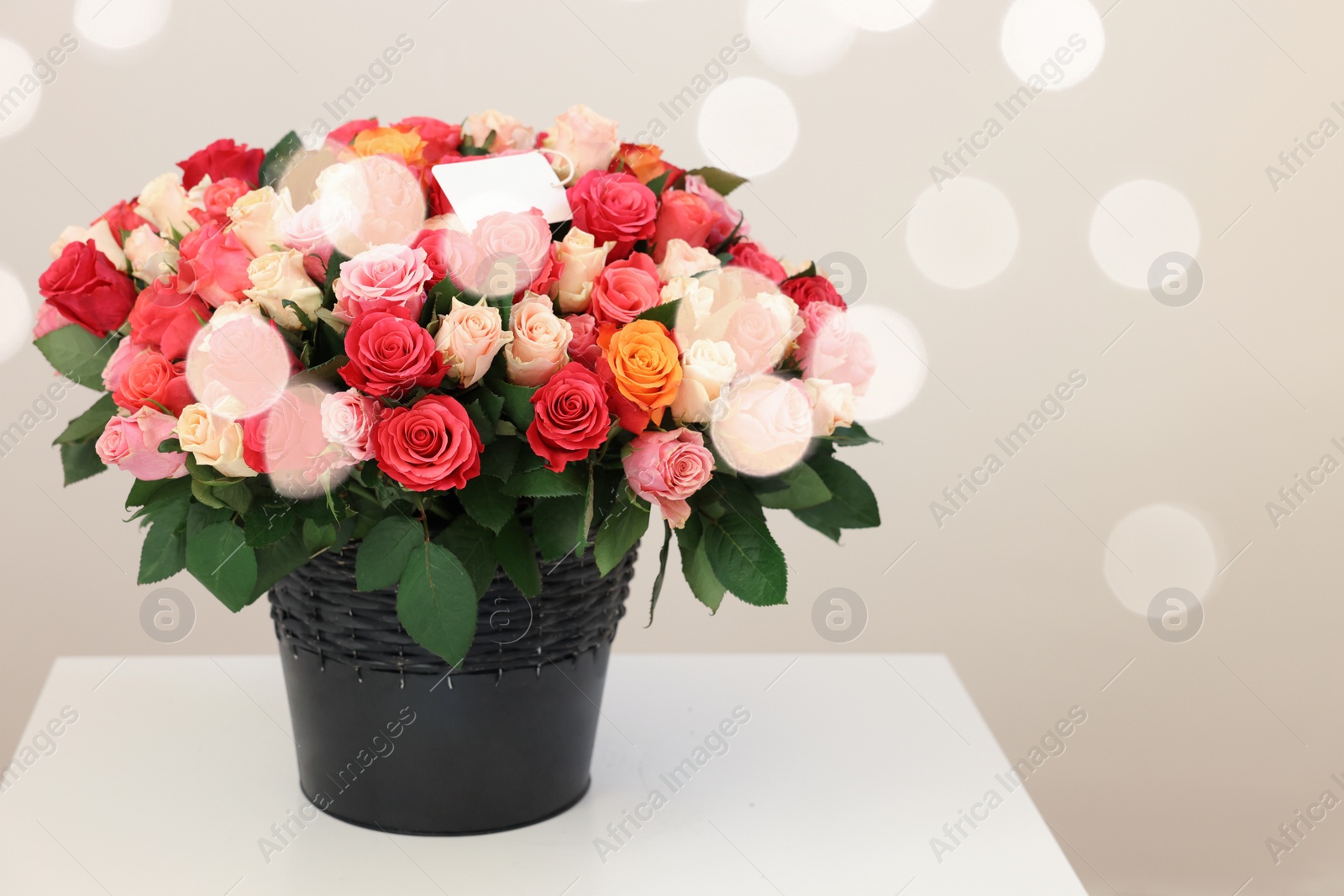 Photo of Bouquet of beautiful roses with blank card on white table against light background, space for text