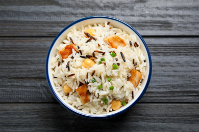 Photo of Delicious rice pilaf with chicken on black wooden table, top view