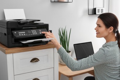 Woman using modern printer at workplace indoors