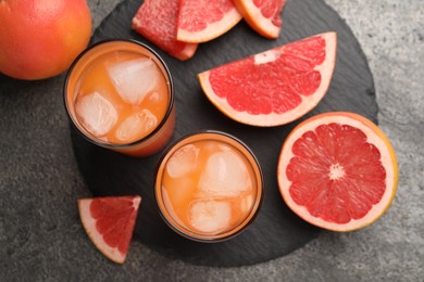 Photo of Tasty grapefruit drink with ice in glasses and fresh fruits on dark textured table, flat lay