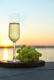 Photo of Glass of champagne and and fresh grapes served near river at sunset