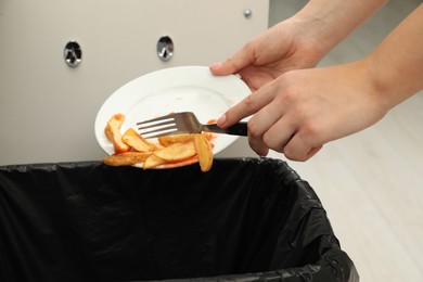 Photo of Woman throwing baked potato with ketchup into bin indoors, closeup