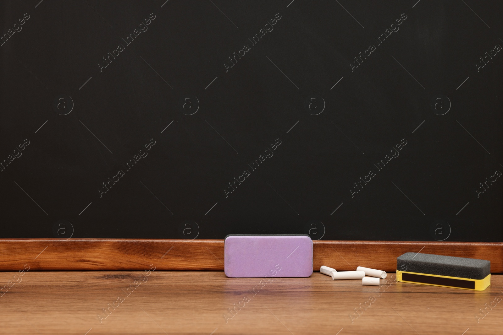 Photo of Pieces of chalk and dusters on wooden table near blackboard, space for text