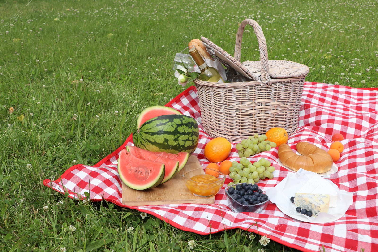 Photo of Picnic blanket with delicious food and wine outdoors on summer day