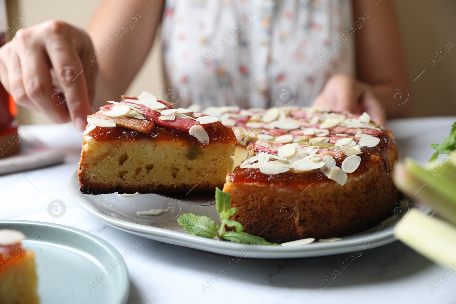 Photo of Woman taking piece of freshly baked rhubarb pie with almond flakes at white marble table, closeup