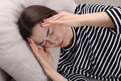 Photo of Sad woman suffering from headache on pillow indoors