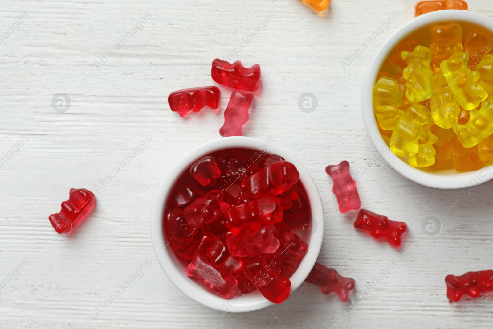 Photo of Bowls with delicious jelly bears on wooden table, flat lay. Space for text