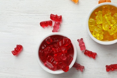 Bowls with delicious jelly bears on wooden table, flat lay. Space for text