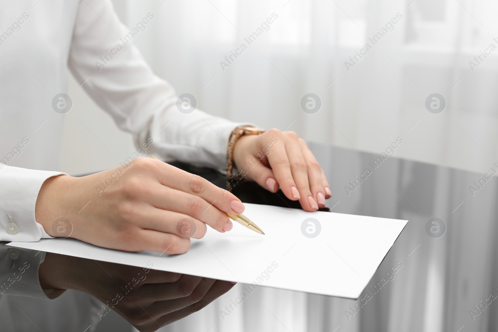 Photo of Woman writing on sheet of paper at glass table, closeup