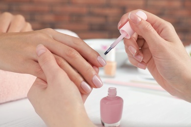 Manicurist applying polish on client's nails at table, closeup. Spa treatment