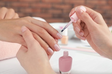 Photo of Manicurist applying polish on client's nails at table, closeup. Spa treatment