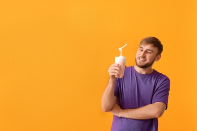 Young man with glass of delicious milk shake on color background