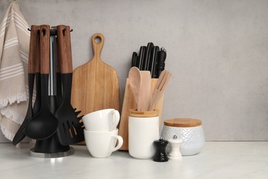 Photo of Set of different kitchen utensils and cups on white near gray wall