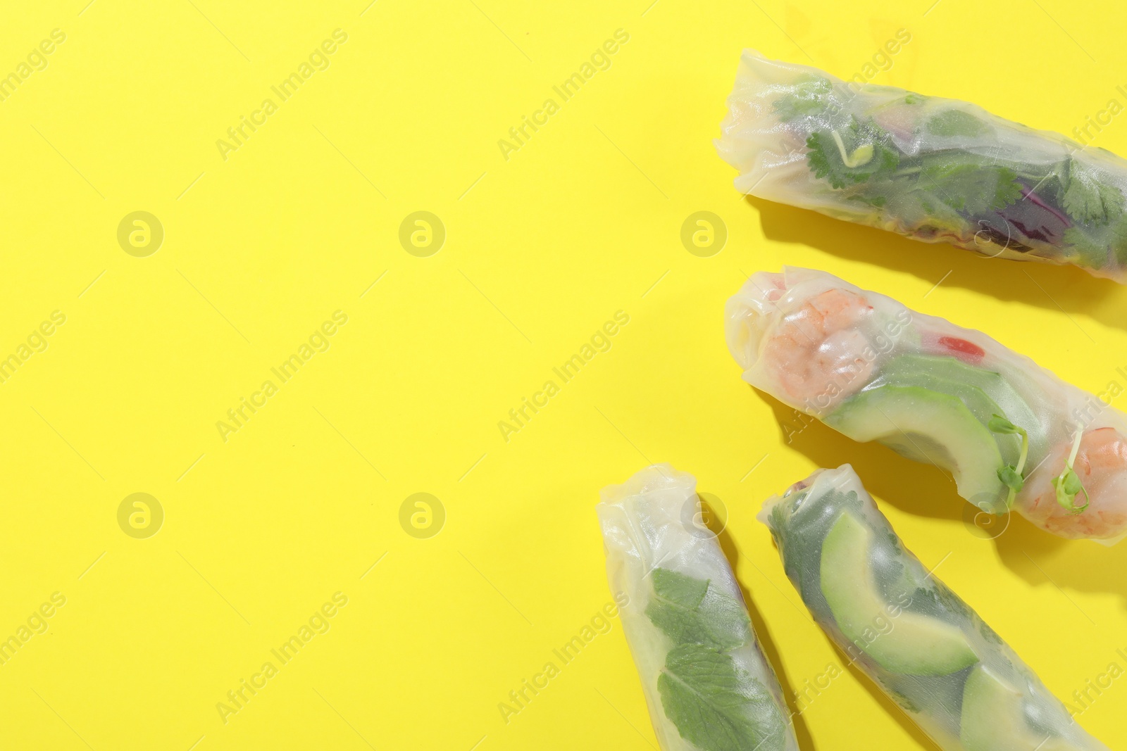 Photo of Delicious spring rolls wrapped in rice paper on yellow background, flat lay. Space for text